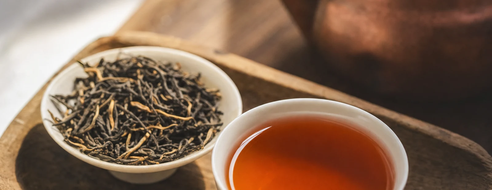 Realistic red tea hero photograph with oxidized leaf strands, copper liquor, and teaware.