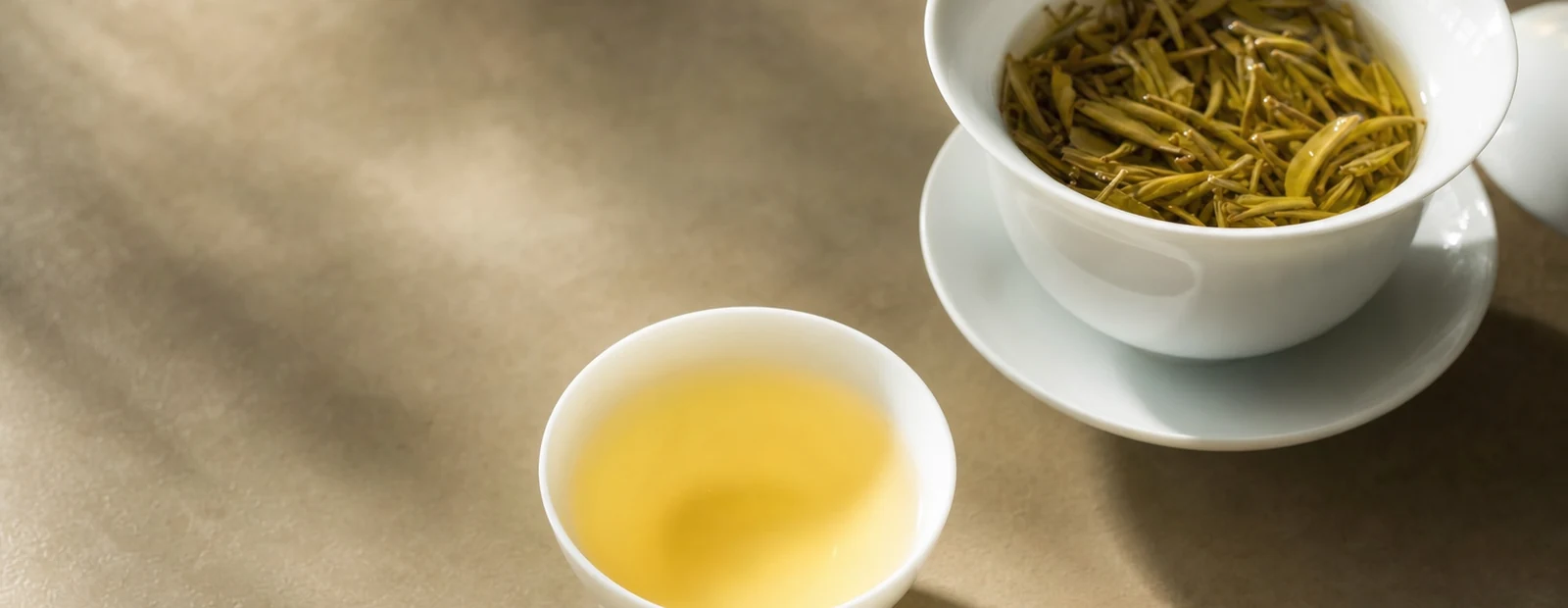 Realistic yellow tea hero photograph with golden liquor, tea leaves, and teaware.